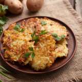 Crispy potato pancakes garnished with parsley on a wooden plate.