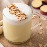 Glass mug with frothy latte on wooden board beside sliced sweet potatoes