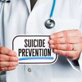 Anonymous doctor in lab coat holding suicide prevention sign