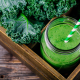 Green kale smoothie in jar with striped straw beside fresh kale leaves