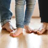 Four pairs of feet, including a child's, standing on a wooden floor.