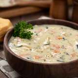 Creamy chicken soup in a wooden bowl, garnished with parsley, beside a biscuit.