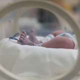 Newborn baby's feet visible through a circular incubator opening.