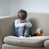 child looking sad with teddy bear on couch