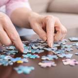 Senior woman playing jigsaw puzzle at home, close up