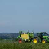 Green tractor spraying crops in a field under a clear blue sky.