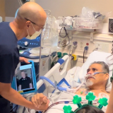 Paul Aguilar is in his hospital bed, with nurse David Yamada standing by his side, grasping his hand. Yamada is also holding a tablet with the message from Sylvester Stallone.