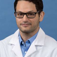 White coat head shot of Cameron Sarabi, giving a small smile at the camera