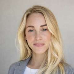 Woman with long blonde hair wearing a gray blazer and a gold necklace.