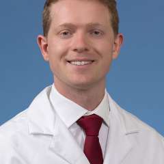 Dr. Sebastian Green in a white coat and tie smiling 