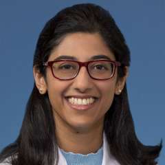 Smiling person in white lab coat and red glasses on blue background.