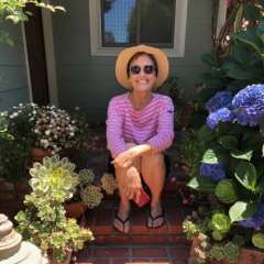 Cindy Stoltman seated on porch steps among potted succulents and blue hydrangeas.