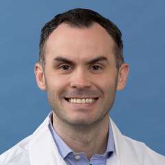 White coat head shot of Daniel Hawkins, smiling at the camera