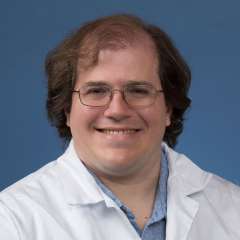 Head shot of Brendan Cohn-Sheehy in white lab coat, smiling at camera