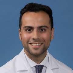 Head shot of Adnan Husein in white lab coat, smiling at camera