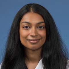 Head shot of Mahima Sukumar in white lab coat, smiling at camera