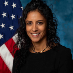 headshot of Dr. Anjani Reddy in black blouse with flag in the background