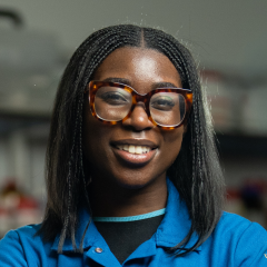 UCLA cancer researcher AJ Addae smiles and stands confidently with arms crossed.