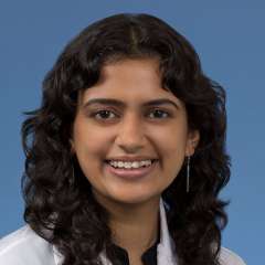 Head shot of Anjali Upadyaya in a white coat, smiling at the camera