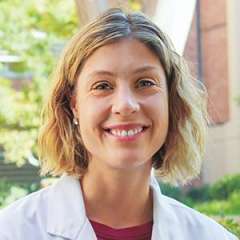 Dr. Annabelle de St. Maurice wearing a lab coat, standing outdoors with greenery in the background.
