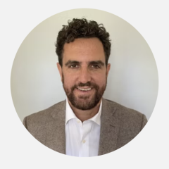 Headshot of a person wearing a blazer and white shirt against a light background.