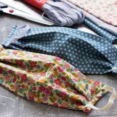 Close-up of colorful fabric face masks with floral and patterned designs, placed on a table with sewing supplies