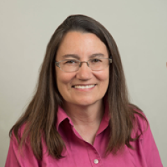 Head-and-shoulders portrait of a person with brown hair wearing a pink shirt