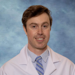 headshot of Dr. Nicholas Kraus in a white lab coat in front of a blue background