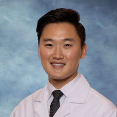 A headshot of Dr. Andy Moon smiling and wearing a white lab coat with a dark tie.