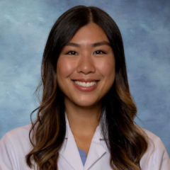 A headshot of Dr. Nicole Nguyen with long brown hair, smiling and wearing a white lab coat. 