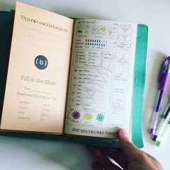 A journal is open to a beige page for owner details and a page with handwritten notes, charts, and colorful symbols, held by a hand.