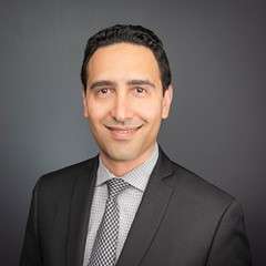 A smiling man with glasses and a grey suit.