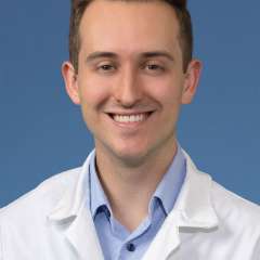 Head shot of Brendan Colgan MD, in white coat, smiling at camera