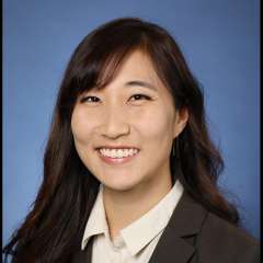 A woman with black hair, wearing a white collared shirt with a blazeer