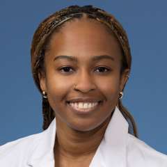 Head shot of Angela Udongwo, MD, MPH, in white coat, smiling at camera