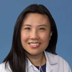 Kara Chew smiling in a white coat against a blue background.