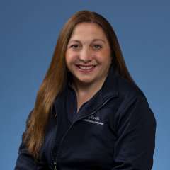 Termeh Toufanian with long hair wearing a navy jacket, sitting against a blue background.