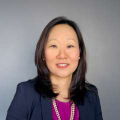 Smiling professional woman wearing blazer and necklace against gray background