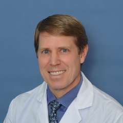 John M. Timmerman, MD wearing a white coat and tie, smiling