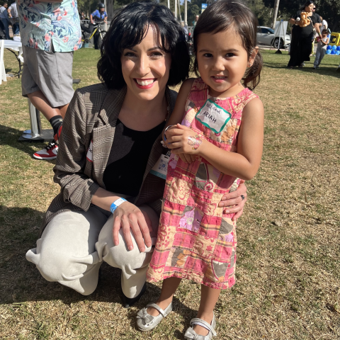 Nurse Rebecca Amrany kneeling down next to a toddler smiling for the camera